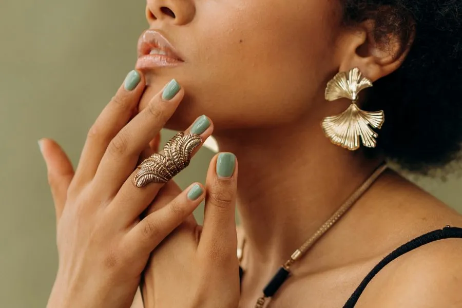 woman with green nail polish touching her face
